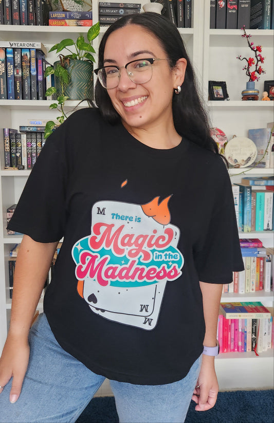 Person wearing a black t-shirt with colorful graphics and text, standing in front of a bookshelf.