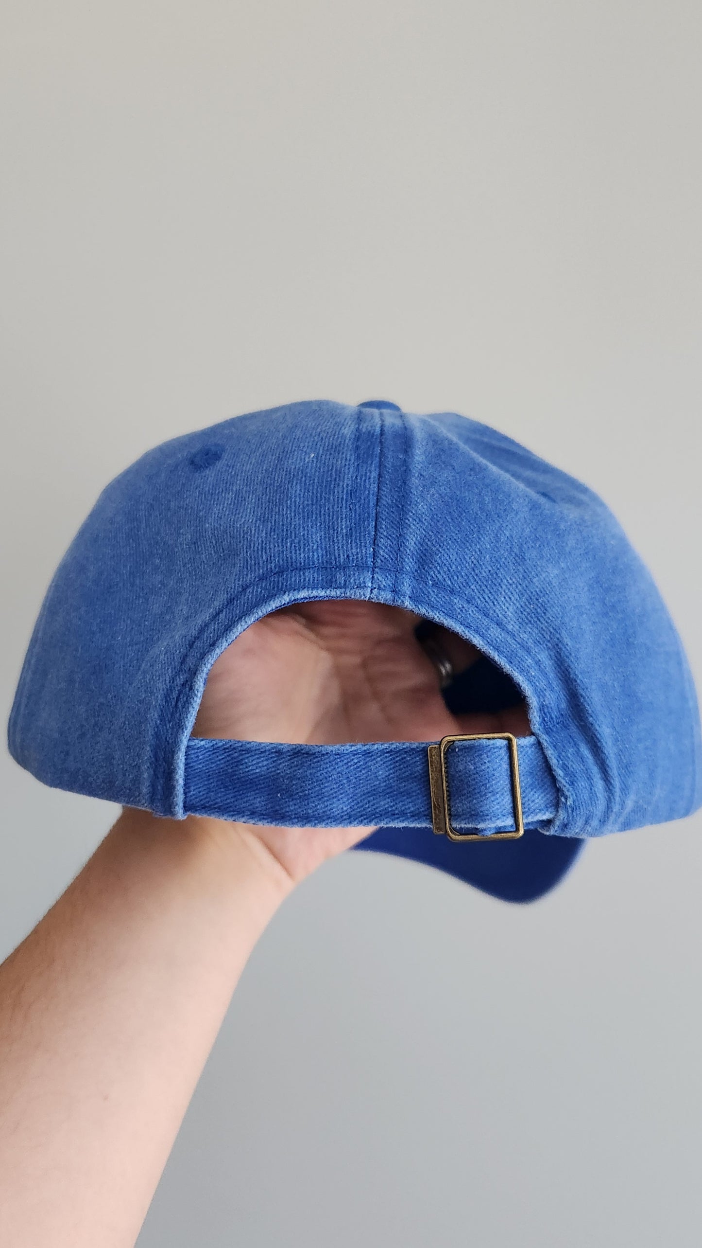 Blue denim cap held by a hand against a gray background