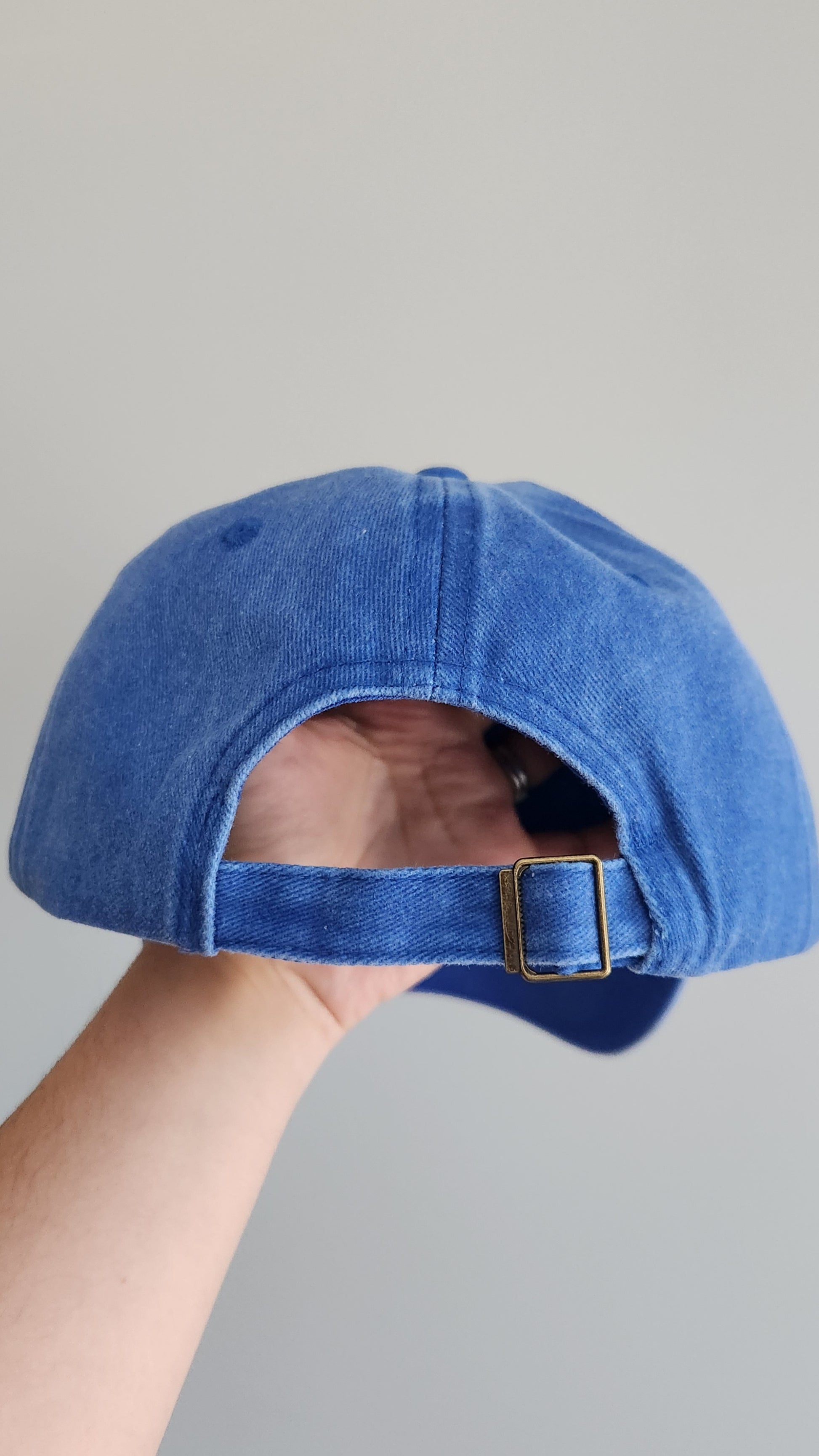 Blue denim cap held by a hand against a gray background